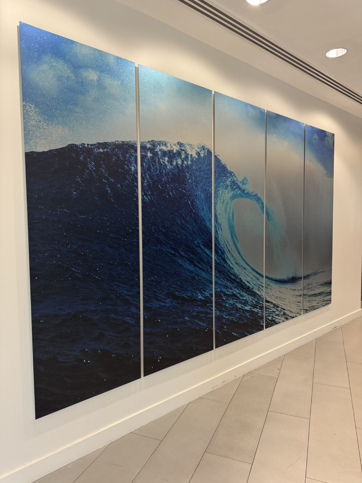 Large multi-panel wall art of a breaking ocean wave in a corridor.
