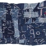 Patchwork fabric with stitched letters and numbers.