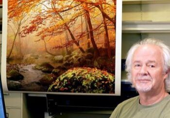 Man sitting next to autumn forest painting.