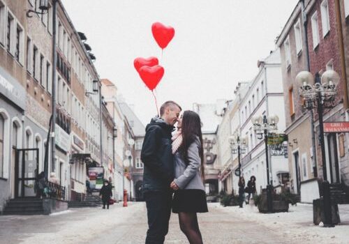 Couple embracing with heart-shaped balloons outdoors.